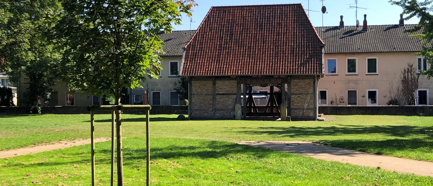 Ältestes Haus Hoya Backsteingebäude mit rotem Ziegeldach und hölzernen Stützen in einer grünen Parklandschaft.