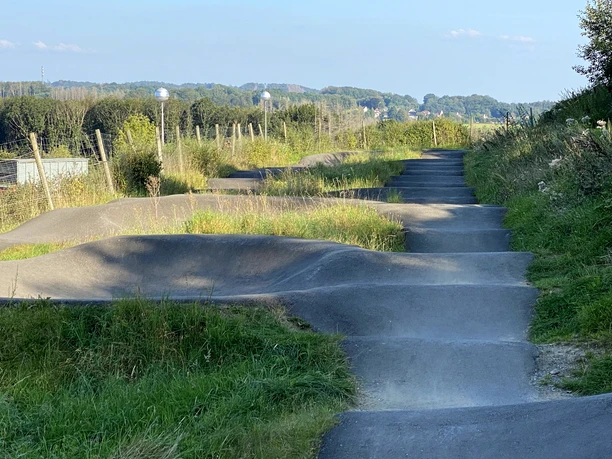 Pumptrack auf :metabolon <p>Pumptrack in Lindlar, umgeben von grünen Wiesen und Bäumen, bei sonnigem Wetter.</p>