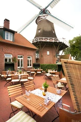 Aussenterrasse Hengstforder Mühle Die Außenterrasse der Hengstforder Mühle zeigt rustikale Holzmöbel vor der beeindruckenden Mühle.