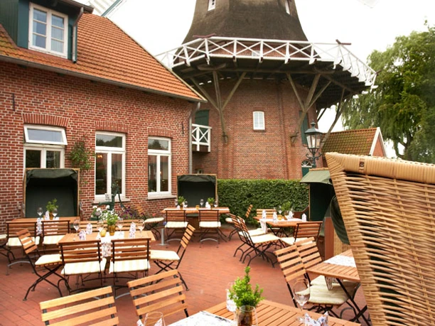 Aussenterrasse Hengstforder Mühle Die Außenterrasse der Hengstforder Mühle zeigt rustikale Holzmöbel vor der beeindruckenden Mühle.