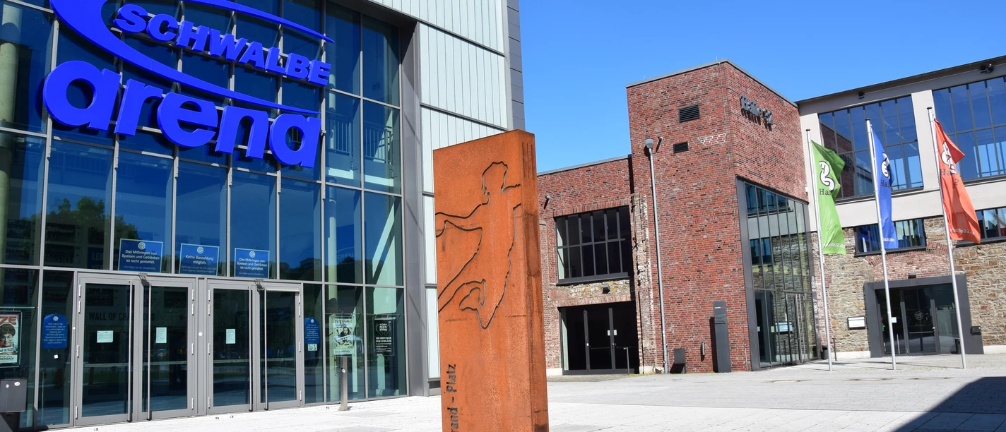 Steinmüllergelände Halle 32 / Schwalbe Arena <p>Die Schwalbe Arena in Gummersbach, eine moderne Halle mit Glasfassade und umliegenden Flaggen.</p>