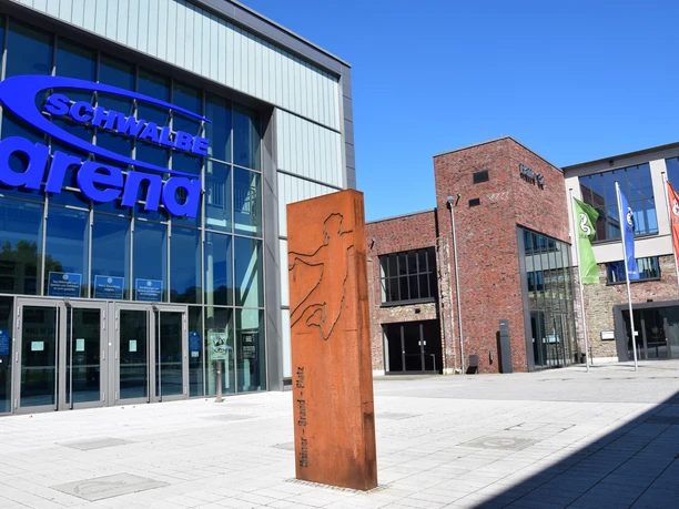 Steinmüllergelände Halle 32 / Schwalbe Arena <p>Die Schwalbe Arena in Gummersbach, eine moderne Halle mit Glasfassade und umliegenden Flaggen.</p>