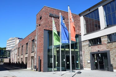 Steinmüllergelände Halle 32 / Schwalbe Arena Halle 32 Gummersbach, modernes Kulturzentrum in einem sanierten Ziegelbau mit bunten Flaggen davor.