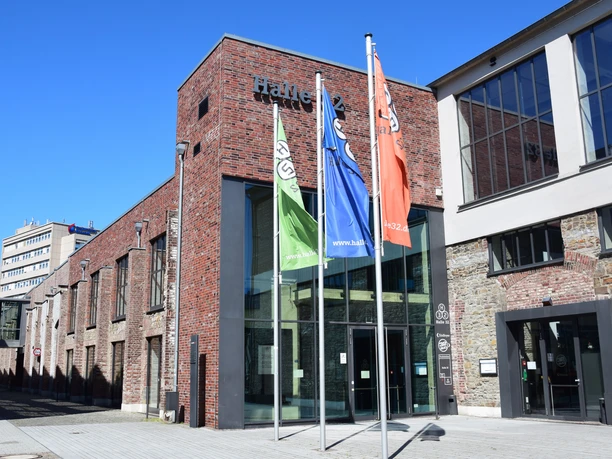 Steinmüllergelände Halle 32 / Schwalbe Arena Halle 32 Gummersbach, modernes Kulturzentrum in einem sanierten Ziegelbau mit bunten Flaggen davor.