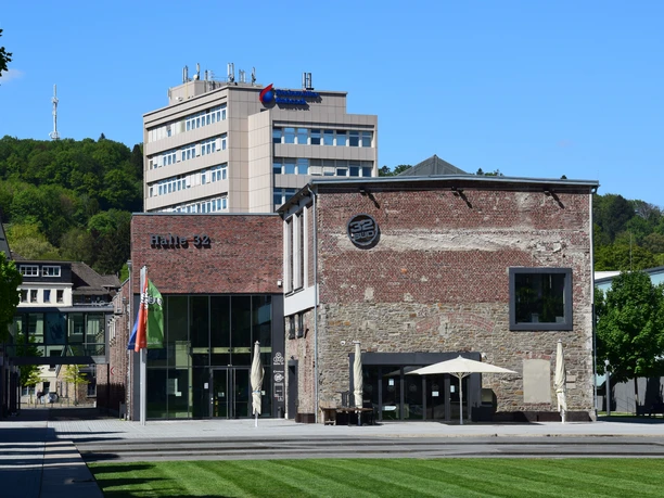 Steinmüllergelände Gummersbacher Kulturzentrum "Halle 32" bei strahlendem Sonnenschein vor grün bewachsenem Hügel.