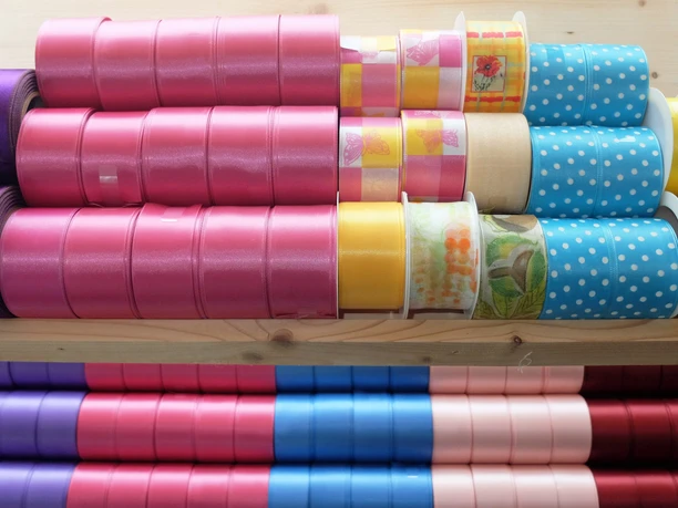 OL_Grossroehrsdorf_MDB_WG_DSCF3167.JPG Verschiedene bunte Stoffbänder in Pink, Blau und Gelb auf Holzregal gestapelt.