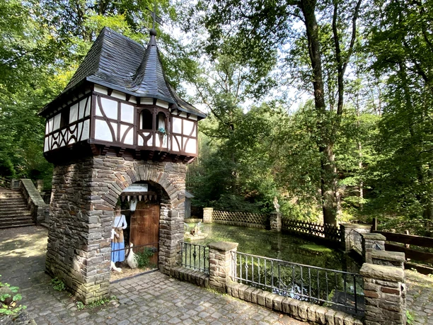 Märchenhafte Kapelle aus Bruchstein und Fachwerk im Wald, mit zierlichen Details und umgeben von Bäumen.