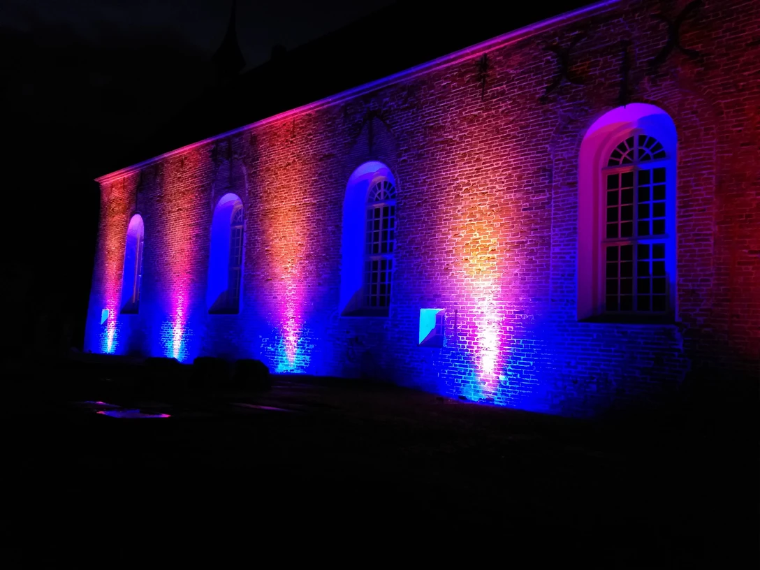 Kirche in Visquard im Lichterglanz Backsteinkirche bei Nacht, farbenprächtig in Blau, Rosa und Orange für die Lichtertage illuminiert.