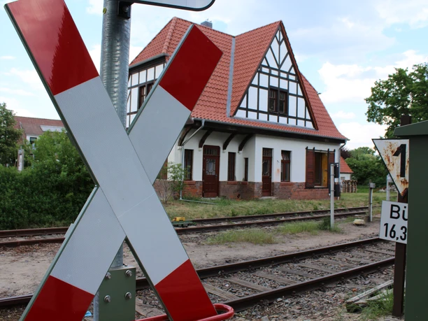 An old half-timbered building with a pitched roof on the railroad track, striking cross in the foreground.