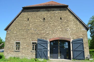 Steinbau mit offenstehenden blauen Holztüren, kleinen Fenstern und einem roten Ziegeldach.