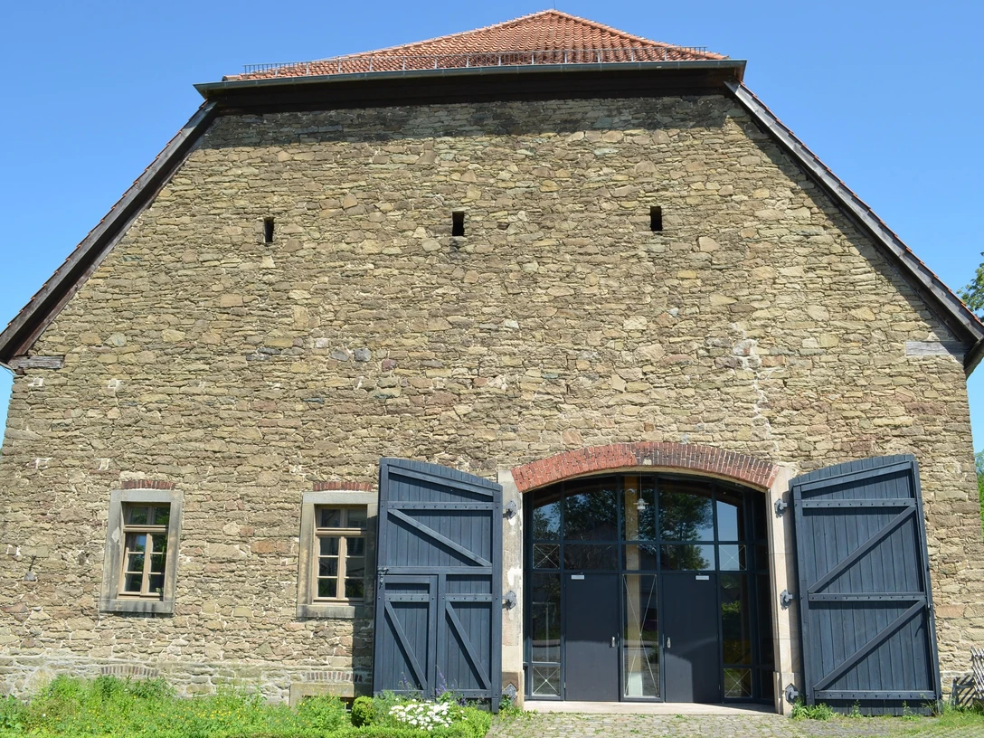 Biologische Station Steinbau mit offenstehenden blauen Holztüren, kleinen Fenstern und einem roten Ziegeldach.