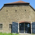 Biologische Station Steinbau mit offenstehenden blauen Holztüren, kleinen Fenstern und einem roten Ziegeldach.