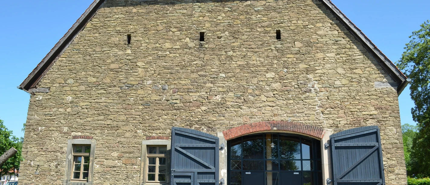 Biologische Station Steinbau mit offenstehenden blauen Holztüren, kleinen Fenstern und einem roten Ziegeldach.