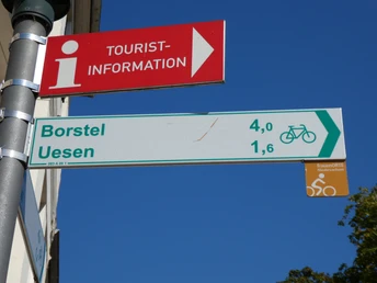 Cato Bontjes van Beek-Radweg Wegweiser zeigt Radrouten-Informationen: Borstel 4 km, Uesen 1,6 km. Blaues Himmelshintergrund.