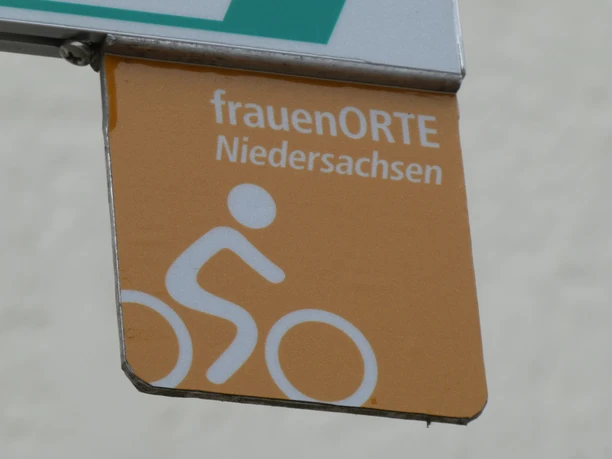 Brown sign of the cycle route frauenORTE Niedersachsen with pictogram of a cyclist on a beige background.