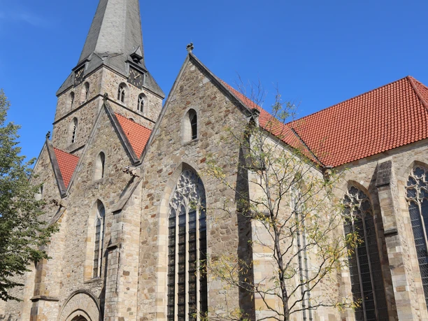 Neugotische Kirche mit hohem Turm und rotem Ziegeldach, umgeben von gepflastertem Platz.
