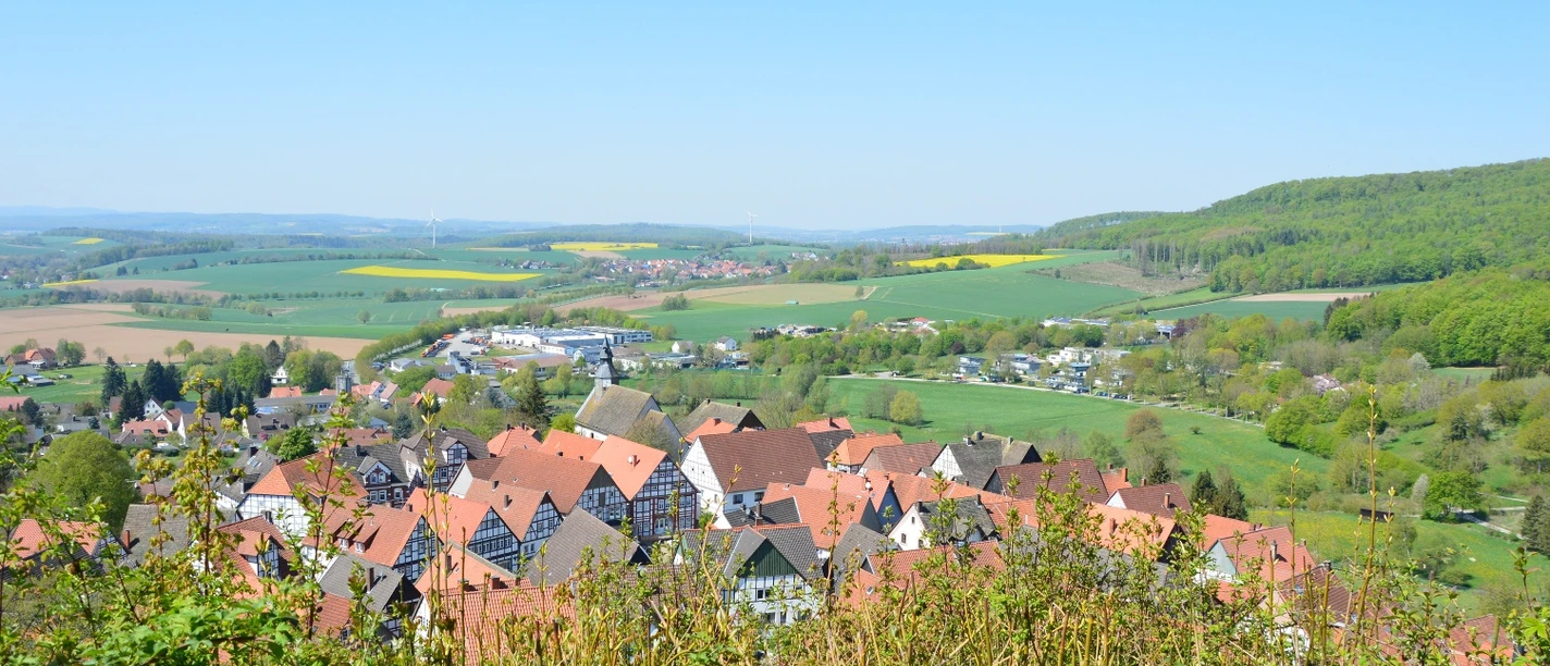 Grafenblick Blick auf ein Dorf mit roten Dächern, umgeben von grünen Hügeln und Feldern unter klarem Himmel.