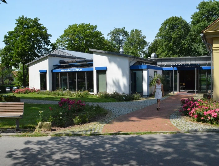 Gesundheitszentrum Ein modernes Gesundheitszentrum mit blauen Vordächern, umgeben von gepflegten Blumenbeeten.