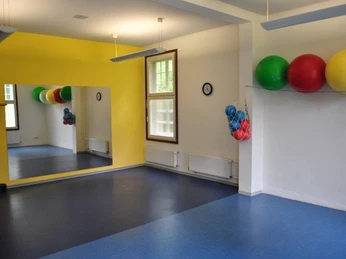 Gymnastikraum Ein heller Raum mit Spiegel, blauen Boden und bunten Gymnastikbällen an der Wand.