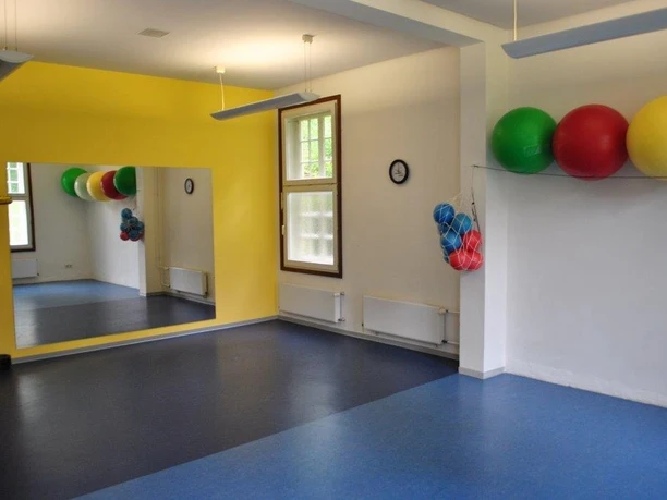 Gymnastikraum Ein heller Raum mit Spiegel, blauen Boden und bunten Gymnastikbällen an der Wand.