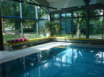 Schwimmbad Großer Innenpool mit klaren blauen Wasser, umgeben von hohen Fenstern und grünen Pflanzen.