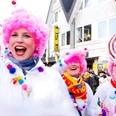 Karneval2015.jpg Menschen in farbenfrohen Kostümen bei einem fröhlichen Karnevalsumzug mit pinken Perücken.