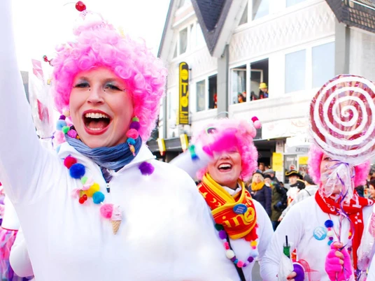 Karneval2015.jpg Menschen in farbenfrohen Kostümen bei einem fröhlichen Karnevalsumzug mit pinken Perücken.