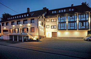 Hotel Goldener Acker Hotelgebäude mit beleuchteter Fassade und großer Fensterfront am Abend, parkender PKW vorne.