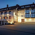 Hotel Goldener Acker Hotelgebäude mit beleuchteter Fassade und großer Fensterfront am Abend, parkender PKW vorne.