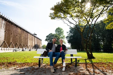 Herrlich zum Ausspannen: Der Kurpark in Bad Rothenfelde A couple sits relaxing on a park bench in front of a graduation wall on a sunny day.