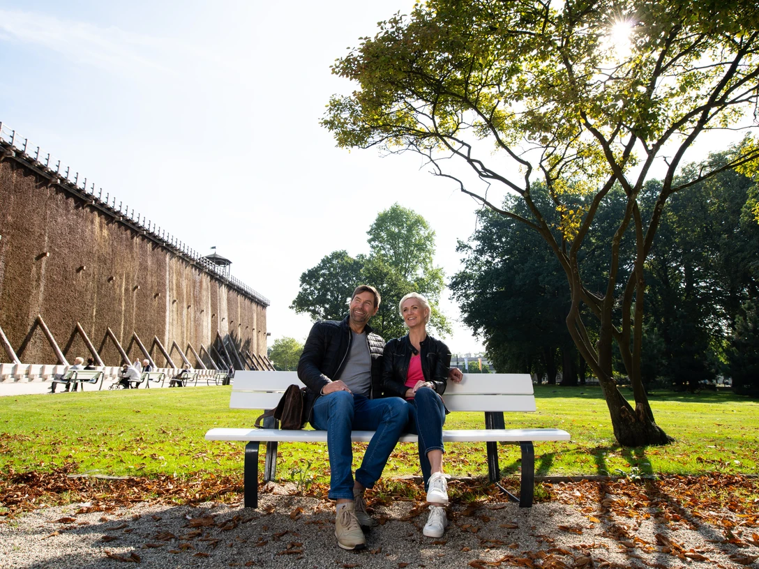 Herrlich zum Ausspannen: Der Kurpark in Bad Rothenfelde Ein Paar sitzt entspannt auf einer Parkbank vor einer Gradierwand an einem sonnigen Tag.A couple sits relaxing on a park bench in front of a graduation wall on a sunny day.Et par sidder og slapper af på en parkbænk foran en gradueringsvæg på en solskinsdag.Een stel zit ontspannen op een bankje in het park voor een afstudeermuur op een zonnige dag.