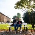 Herrlich zum Ausspannen: Der Kurpark in Bad Rothenfelde Ein Paar sitzt entspannt auf einer Parkbank vor einer Gradierwand an einem sonnigen Tag.A couple sits relaxing on a park bench in front of a graduation wall on a sunny day.Et par sidder og slapper af på en parkbænk foran en gradueringsvæg på en solskinsdag.Een stel zit ontspannen op een bankje in het park voor een afstudeermuur op een zonnige dag.