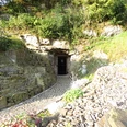 Eingang zum Eiskeller Eingangsportal einer Höhle in steiler Felswand, umgeben von üppigem Grün; gepflasterter Eingang.