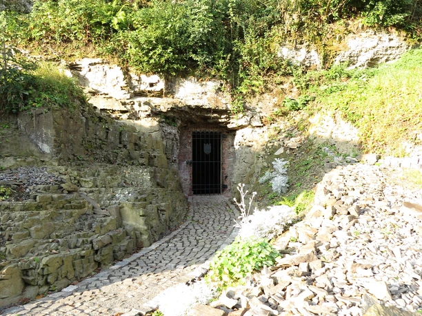 Eingang zum Eiskeller Eingangsportal einer Höhle in steiler Felswand, umgeben von üppigem Grün; gepflasterter Eingang.