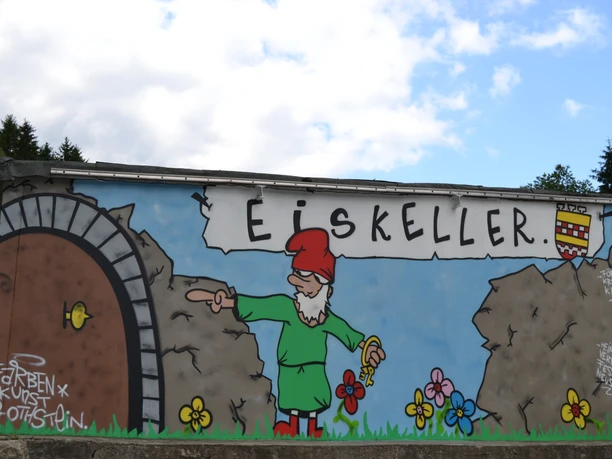 Heinzelmänchen-Graffiti am Eingang zum Eiskeller Eine bunte Wandmalerei zeigt einen Zwerg als Wegweiser am Eingang zu einem Eiskeller.