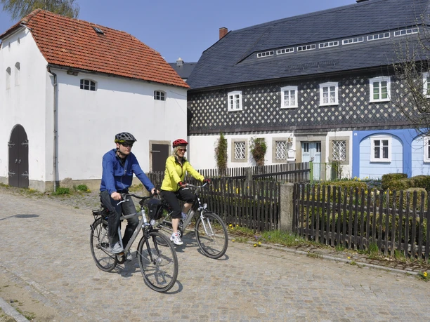 Two cyclists in front of traditional half-timbered houses in a quiet street in Upper Lusatia.