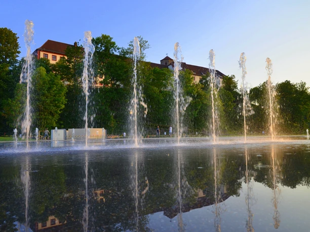 Der Kneipp-Erlebnispark in Bad Iburg am Abend Springbrunnen mit Wasserspielen und Spiegelung, Bäume und Gebäude im Hintergrund bei Sonnenuntergang.