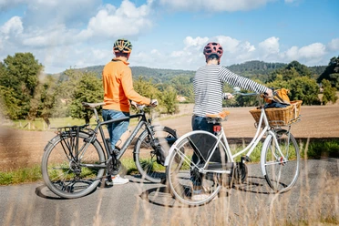 Schöne Aussichten auf der Grenzgängerroute Zwei Radfahrer betrachten eine ländliche Landschaft auf einem asphaltierten Weg.