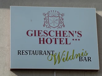 The picture shows a sign with the inscription Gieschen's Hotel and Restaurant Wildnis Bar in an elegant design.