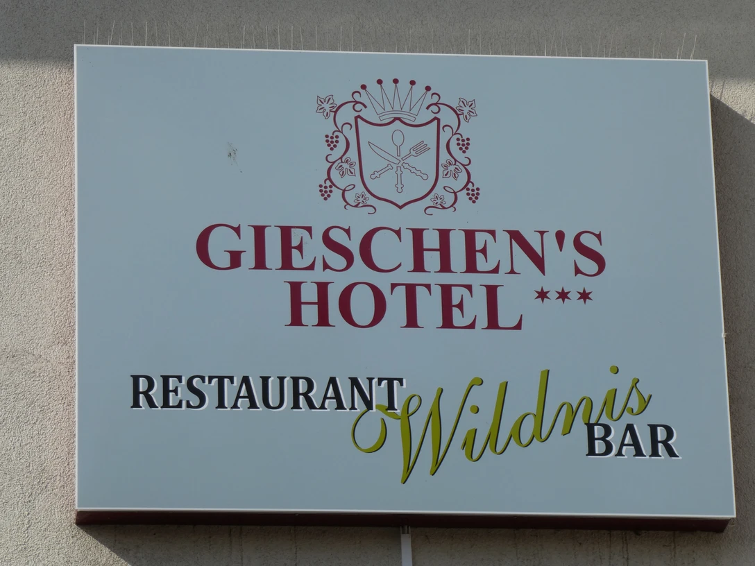 Das Bild zeigt ein Schild mit der Aufschrift Gieschen's Hotel und Restaurant Wildnis Bar in elegantem Design.