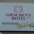 Das Bild zeigt ein Schild mit der Aufschrift Gieschen's Hotel und Restaurant Wildnis Bar in elegantem Design.