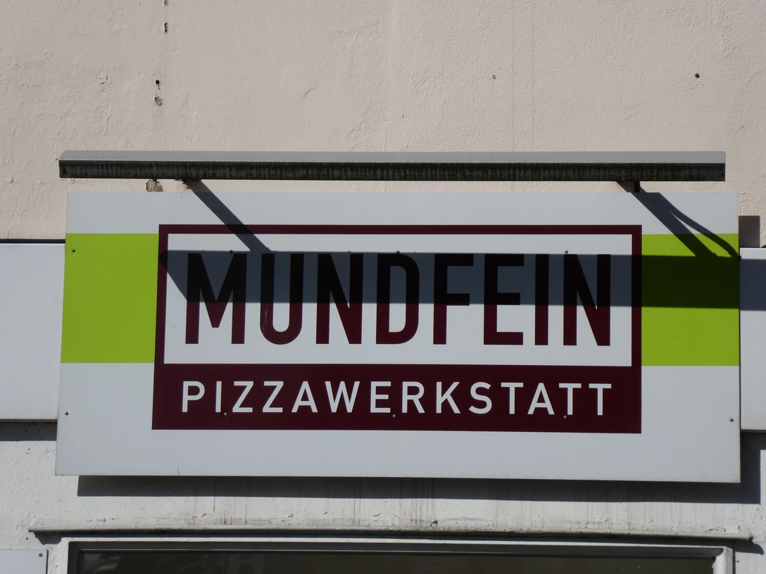 Mundfein Schild mit Aufschrift "Mundfein Pizzawerkstatt" auf hellen Hintergrund, mit modernem Design.Sign with the inscription "Mundfein Pizzawerkstatt" on a light background, with a modern design.Skilt med påskriften "Mundfein Pizzawerkstatt" på en lys baggrund, med et moderne design.Bord met de inscriptie "Mundfein Pizzawerkstatt" op een lichtgekleurde achtergrond, met een modern ontwerp.