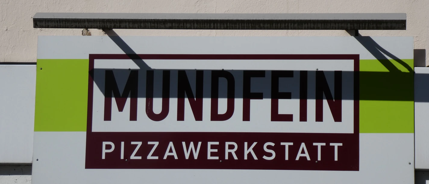 Mundfein Schild mit Aufschrift "Mundfein Pizzawerkstatt" auf hellen Hintergrund, mit modernem Design.