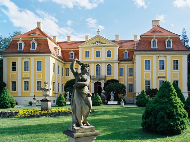 Barockschloss Rammenau Barockschloss Rammenau in gelb mit rotem Dach, zentrale Statue im gepflegten Garten.