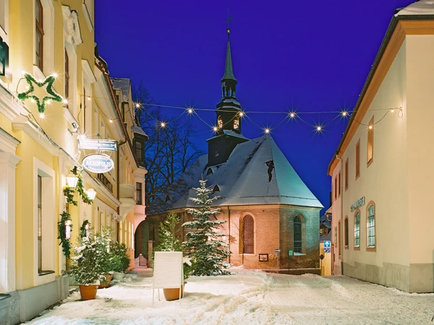 Bergkirche, Annaberg-Buchholz Eine beleuchtete Kirche im Schnee, umgeben von festlich dekorierten Gebäuden.