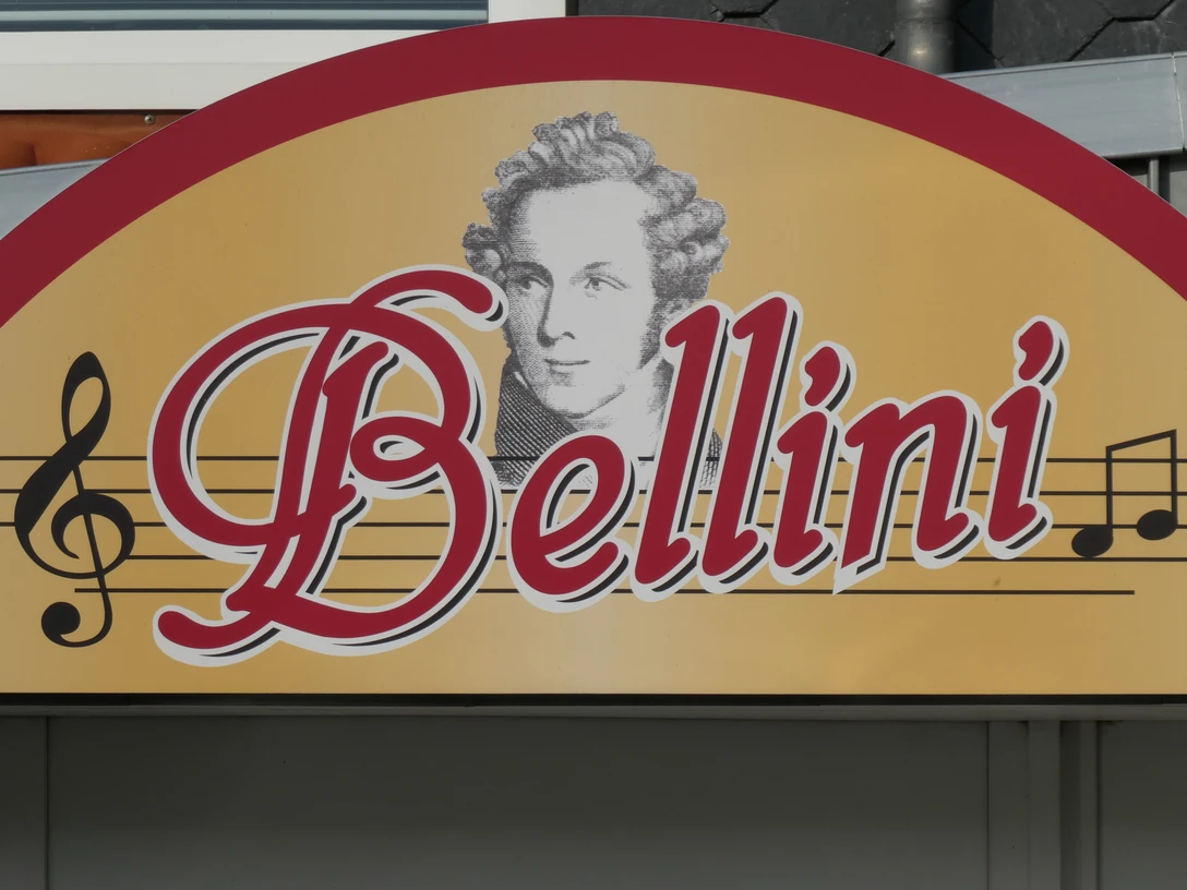 Restaurant Bellini Restaurant Bellini: Logo auf gelbem Schild mit Notenlinien und Porträt von Komponist Vincenzo Bellini.