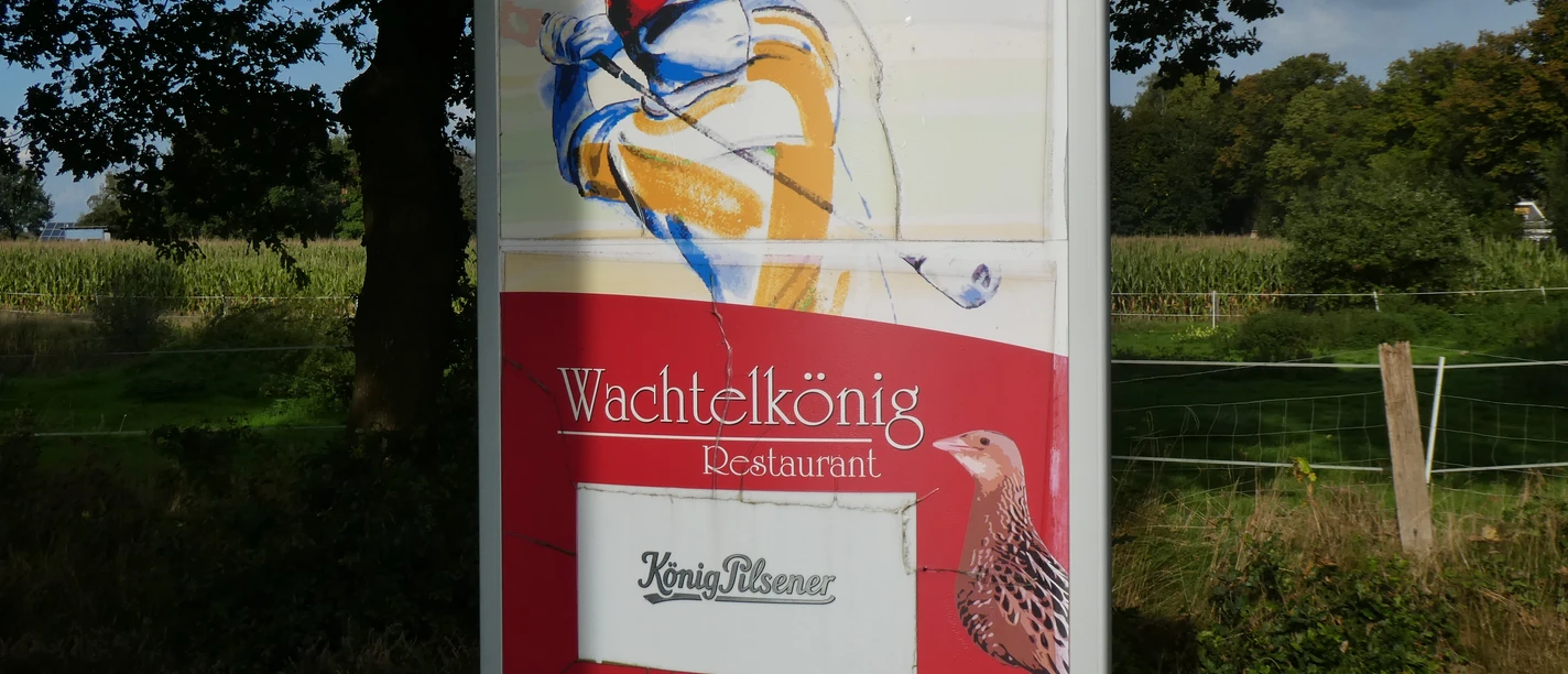 A sign with the words "Golf in Achim" and "Wachtelkönig Restaurant", surrounded by nature.