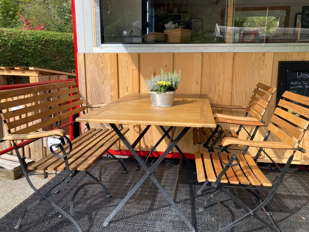 Gedeckte Sitzplätze vor Barwagen Holztisch mit vier Sitzgelegenheiten und Blümchen-Deko