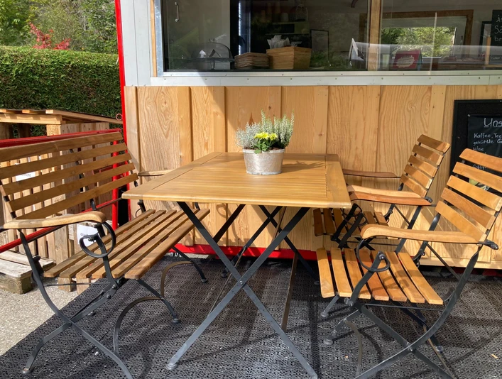 Places assises couvertes devant le chariot-bar Holztisch mit vier Sitzgelegenheiten und Blümchen-DekoWooden table with four seats and floral decorationTable en bois avec quatre sièges et décoration de fleurs
