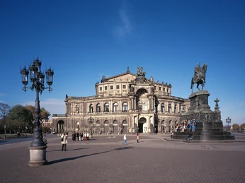 Semperoper, Dresden Von 1838 bis 1841 errichtete der Baumeister Gottfried Semper (18031879) ein neues koenigliches Hoftheater, welches allerdings schon am 21. September 1869 einem Brand zum Opfer fiel. Schon bald wurde von Gottfried Semper ein zweites Gebaeude entworfen, das unter Leitung seines aeltesten Sohnes Manfred Semper (18381913) von 1871 bis 1878 am Theaterplatz erbaut wurde. Der Theaterbau verfuegt über eine prachtvolle Innenausstattung. Ueber dem Portal erhebt sich eine bronzene Pantherquadriga mit Dionysos und Ariadne von Johannes Schilling. Die Westfassade der Hinterbühne zieren das sächsische Wappen, die Figuren Liebe und Gerechtigkeit sowie ein Kopf Gottfried Sempers. Neben dem Eingang stehen die Skulpturen von Johann Wolfgang von Goethe und Friedrich Schiller, in den Seitennischen der Fassade die von William Shakespeare, Sophokles, Molière und Euripides. Dieser zweite Bau fiel in der Schreckensnacht des 13. Februar 1945 dem Luftangriff auf Dresden zum Opfer. Nach dem Zweiten Weltkrieg bereiteten 19461955 Sicherungsarbeiten sowie konzeptionelle Studien 19681976 den Wiederaufbau vor. Am 24. Juni 1977 erfolgte die Grundsteinlegung und der Wiederaufbau unter der Leitung von Chefarchitekt Wolfgang Hänsch. Anlaesslich des 40. Jahrestages der Zerstoerung konnte am 13. Februar 1985 die Semperoper mit Carl Maria von Webers Oper Der Freischuetz symbolisch wiedereröffnet werden es war diese Oper, mit der das Opernhaus am 31. August 1944 geschlossen worden war. Obwohl sie schon Staatsoper war, erhielt die Oper zusaetzlich nach der Wende den offiziellen Titel Saechsische Staatsoper.